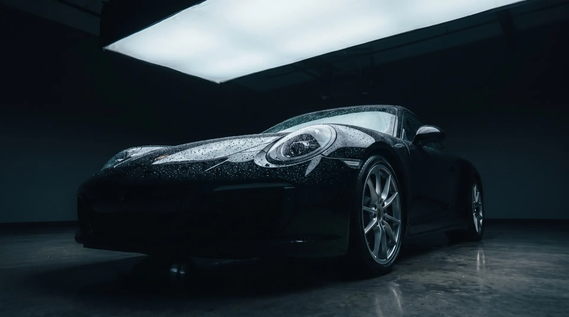 Black sports car under studio light with water beading on the paint